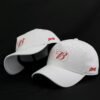 Dois bonés brancos com estampa da Budweiser na lateral e logo na parte frontal. O logo é composto pela letra B em letras decorativas e um símbolo de uma bola de futebol.